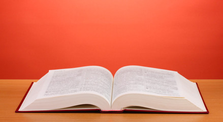 Open book on wooden table on red background
