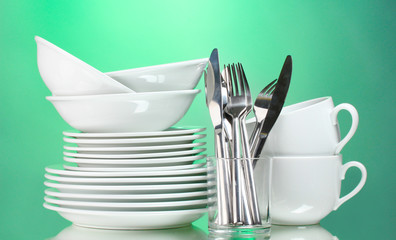 Clean plates, cups and cutlery on green background