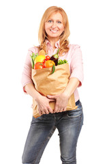 A smiling woman holding a paper bag full of groceries