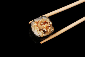 Holding roll with chopsticks isolated on black