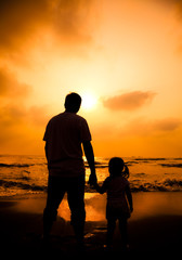 the silhouette of father holding little girl's hand on the beach