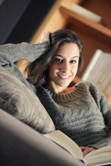 Portrait of a happy young woman lying on couch with book