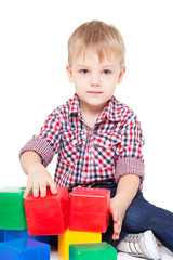 Fototapeta premium little boy sits on a floor and plays with multi-coloured cubes