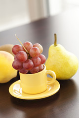 peach, pear, grapes in a cup and saucer on a wooden table