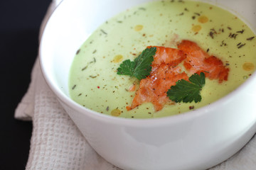 Avocado soup with fried salmon slices in a white soup bowl