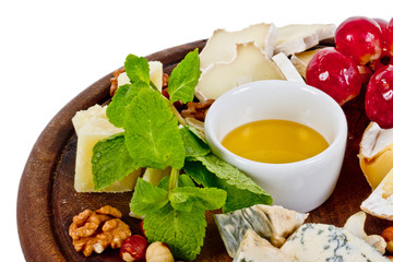 Various types of cheese with honey, nuts and grapes on plate, is