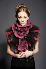 Portrait of a beautiful young woman wearing fur coat. Over gray