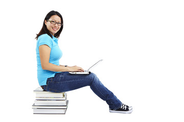 Studentin sitzt auf Bücherstapel mit Laptop