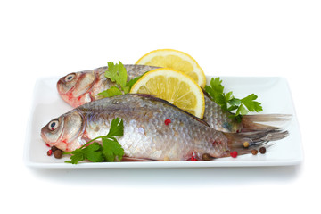 Fresh fishes with lemon and parsley on plate isolated on white