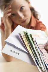 Verzweifelte Frau hält Geld und Rechnung in der Hand