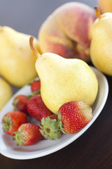 strawberry  in plate, pear and peach on a wooden table