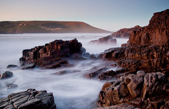 long exposure image of island and black rocks with blurred ocean