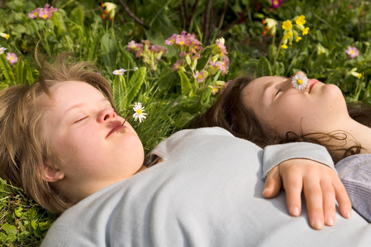 A girl with Down syndrome and her sister resting in the grass.
