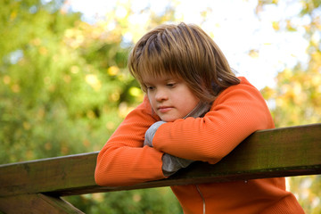 A girl with Down syndrome leaning on a wooden bridge.