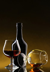 Glasses of brandy and bottle on yellow background