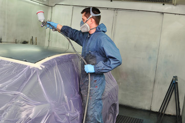 Worker painting a car roof in a paint booth.