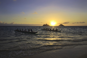 Obraz premium outrigger canoes paddle out from shore at sunrise