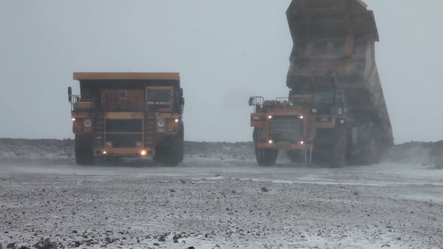 Heavy mining dump trucks unload ore