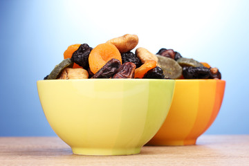 Dried fruits in bright bowls on wooden table on blue background