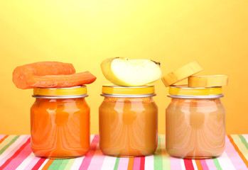 Jars of baby puree on napkin on yellow background