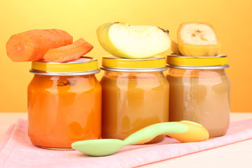 Jars of baby puree with spoon on napkin on yellow background