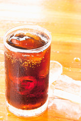 glass of cola with ice on the wooden floor