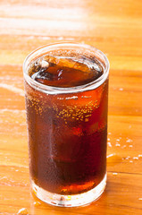 glass of cola with ice on the wooden floor