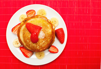 golden buttermilk pancakes with strawberry and banana on red