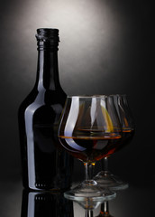 Glasses of brandy and bottle on gray background