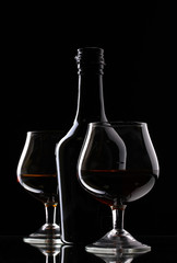 Glasses of brandy and bottle on black background