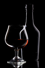 Glass of brandy and bottle on black background