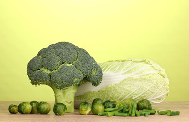 Fresh broccoli and cabbages on wooden table on green background