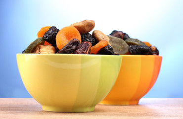 Dried fruits in bright bowls on wooden table on blue background