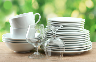 Clean dishes on wooden table on green background