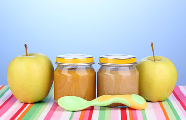Jars of baby puree with spoon on napkin on blue background