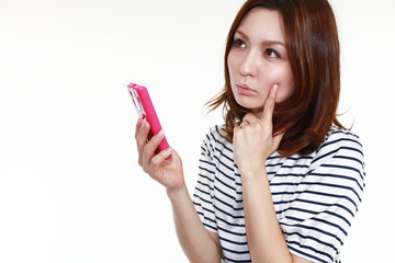 スマートフォンを持ち考え込む女性
