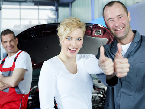 Mechanic and woman in front of car and worker show thumb up