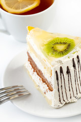 A cup of tea and a piece of tasty creamy cake with fruits