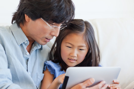 Father and daughter using digital tablet while sitting at home