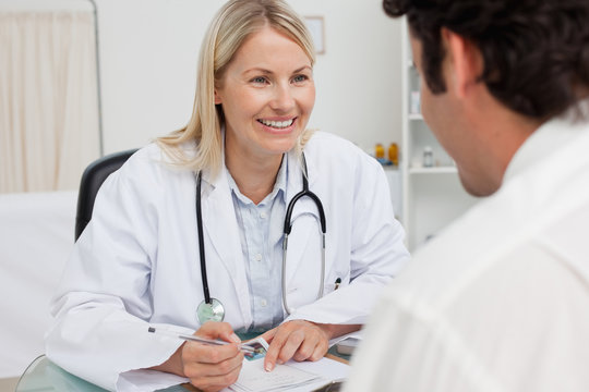 Smiling doctor taking notes while listening to patient