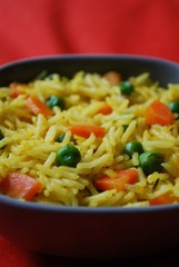 A bowl of yellow basmati rice with carrots, peas and curry