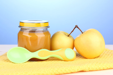 Jar of baby puree with spoon on napkin on blue background