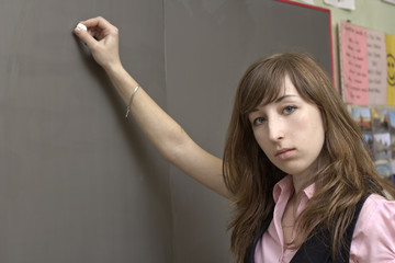 The young beautiful woman writes a chalk on a school board