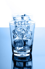 Glasses with crystal clear ice cubes on glossy background