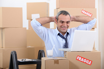 Man surrounded by cardboard boxes using his laptop