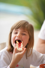 Little girl eating bread with jam on it