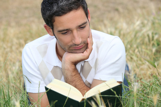young man lying on the grass and reading a book