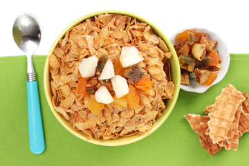tasty cornflakes in bowl with dried fruits on green napkin