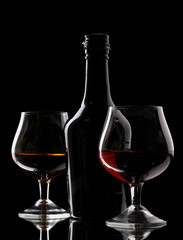 Glasses of brandy and bottle on black background