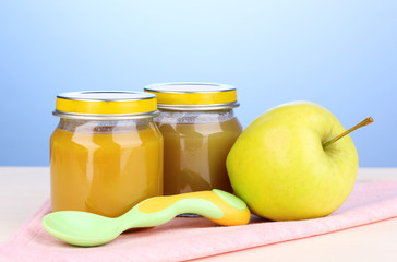 Jars of baby puree with spoon on napkin on blue background